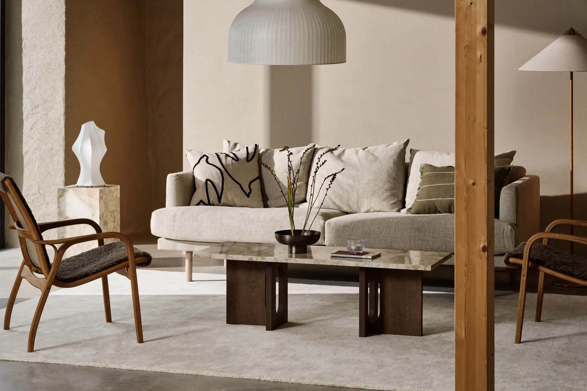 Acogedora sala con sofá beige, mesa de centro de mármol, sillones de madera y lámpara colgante estriada.