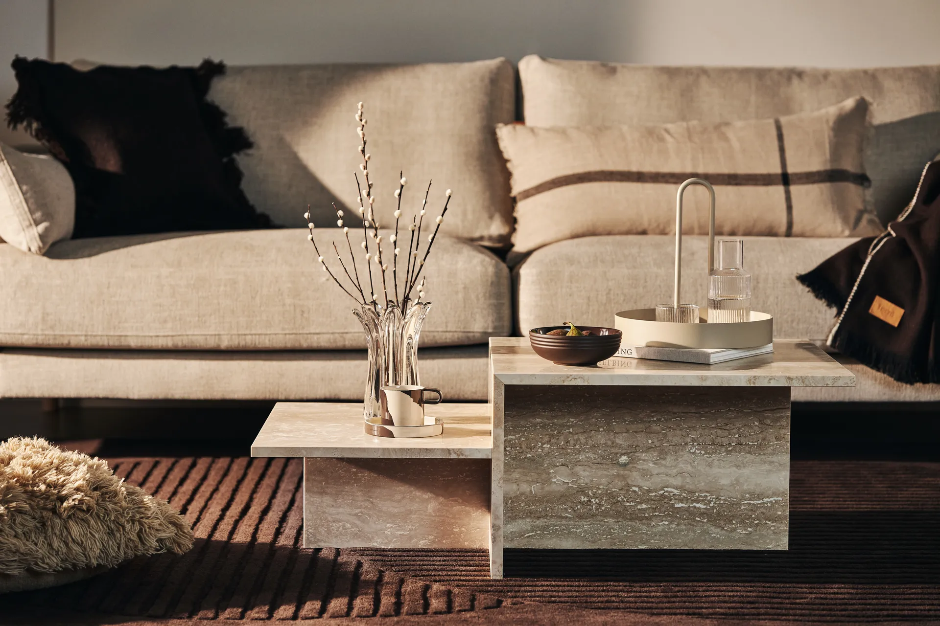 Mesa de centro escalonada de piedra beige frente a un sofá neutro con accesorios decorativos.