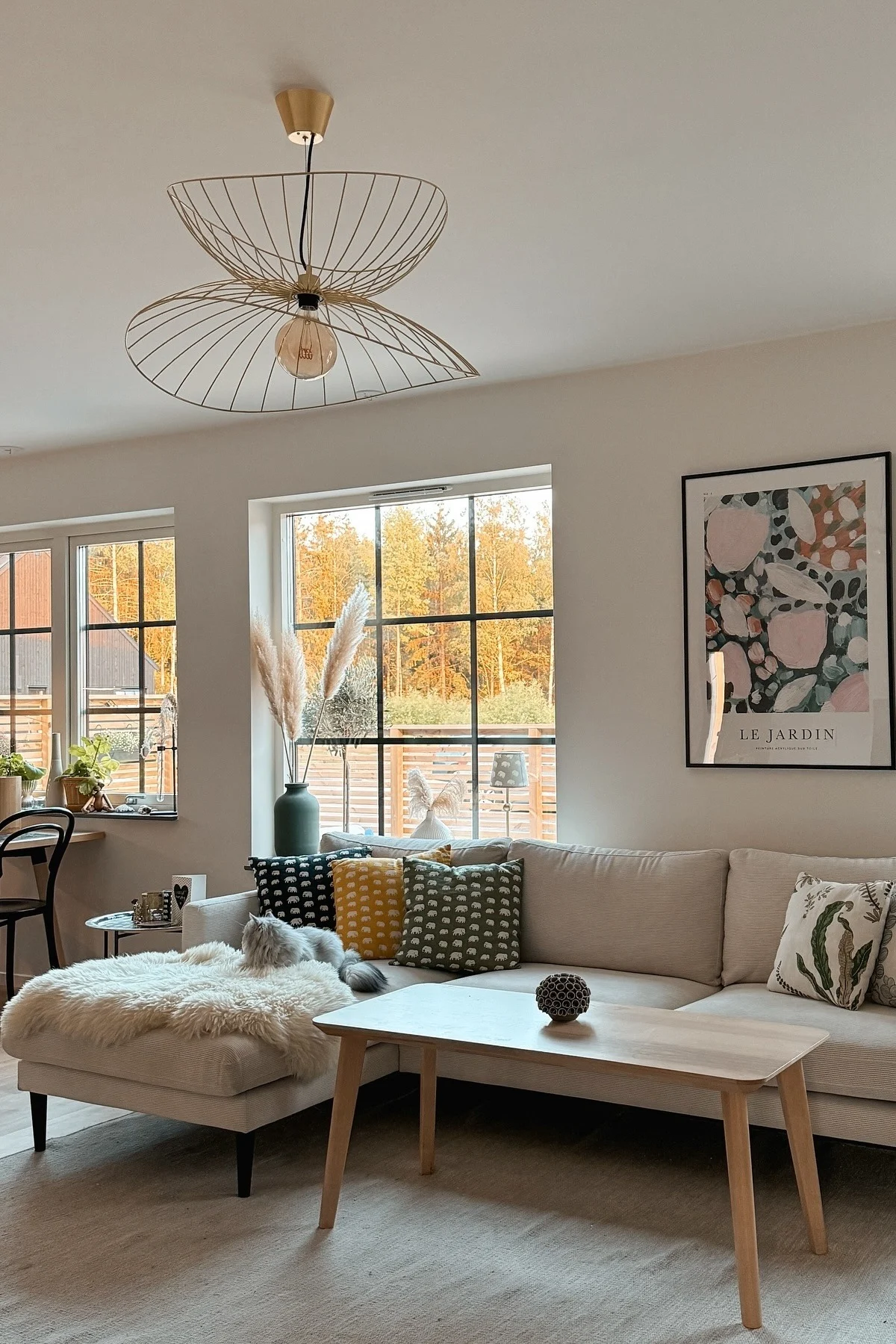 En un alegre salón de estilo escandinavo con sofá, mesa de centro y grandes ventanas, cuelga la lámpara de techo Ray de Globen Lighting.