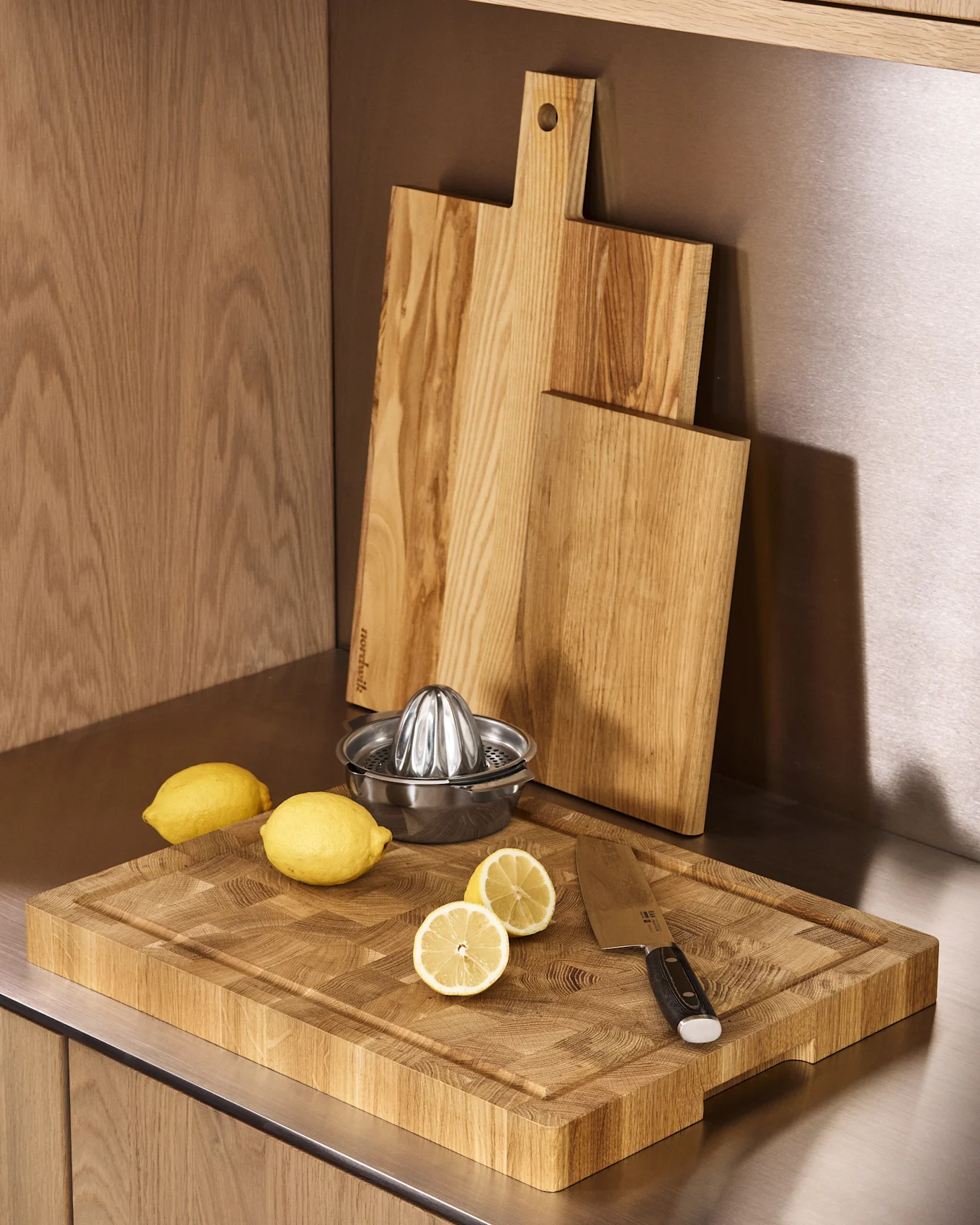 Tres tablas de cortar de madera, un exprimidor de cítricos de acero inoxidable, limones enteros y partidos en una encimera de cocina.