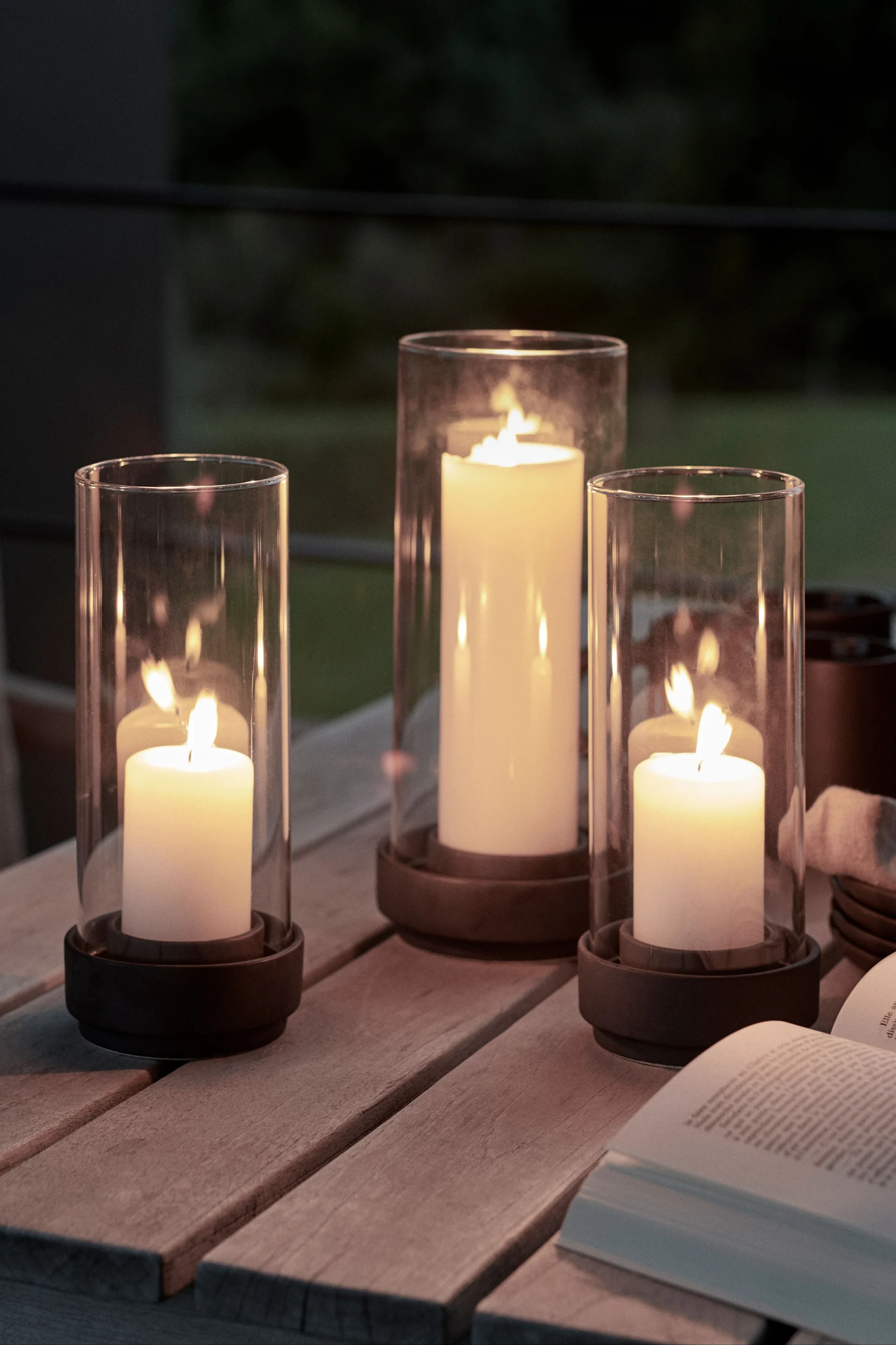 Decora tu mesa de jardín con farolillos de exterior y portavelas de varios tamaños para aumentar el efecto acogedor. Los portavelas Hurricane de Stelton son especialmente adecuados para este fin.