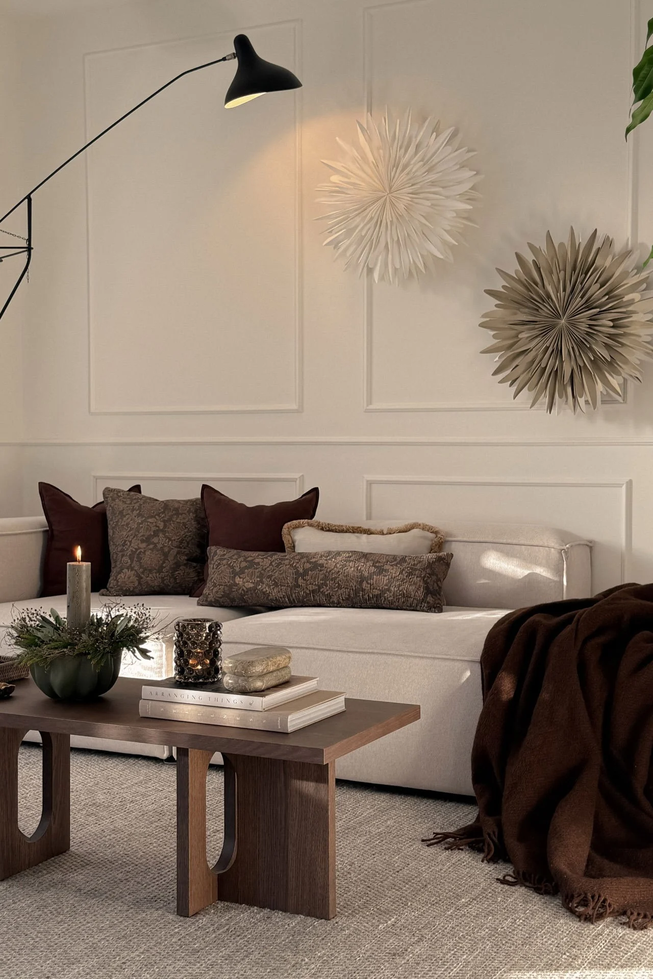 Acogedora sala de estar con sofá crema, mesa de café de madera oscura, velas encendidas, manta marrón y decoraciones de pared de estrellas.