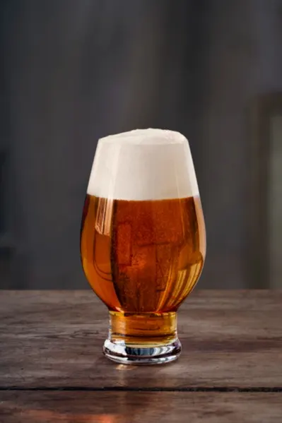Vaso con forma de tulipán de cerveza ámbar con una espuma blanca espesa sobre una mesa de madera rústica.