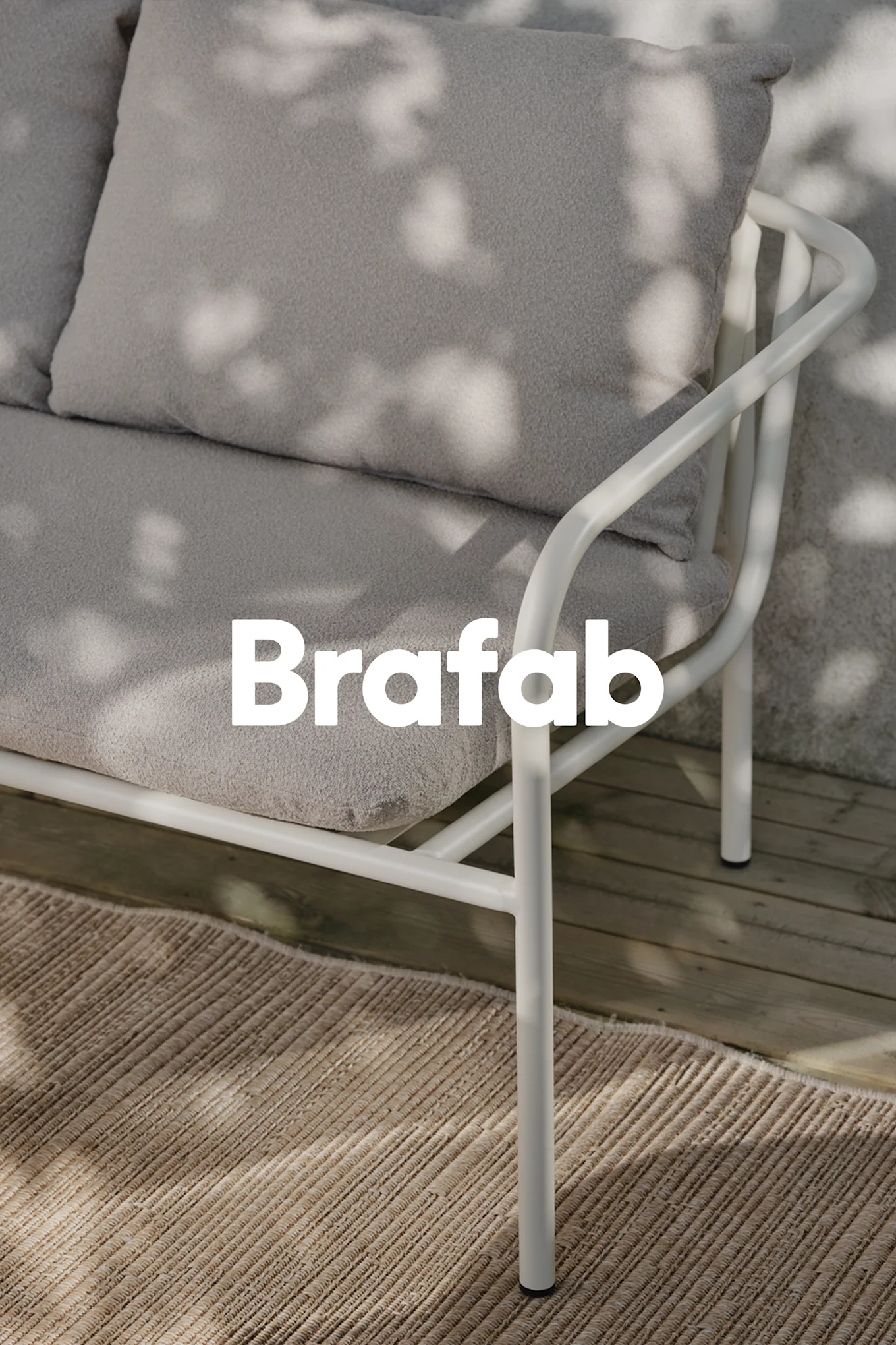 Logo Brafab sobre sofá exterior gris claro con estructura metálica blanca, en alfombra beige sobre tarima de madera con sombras.