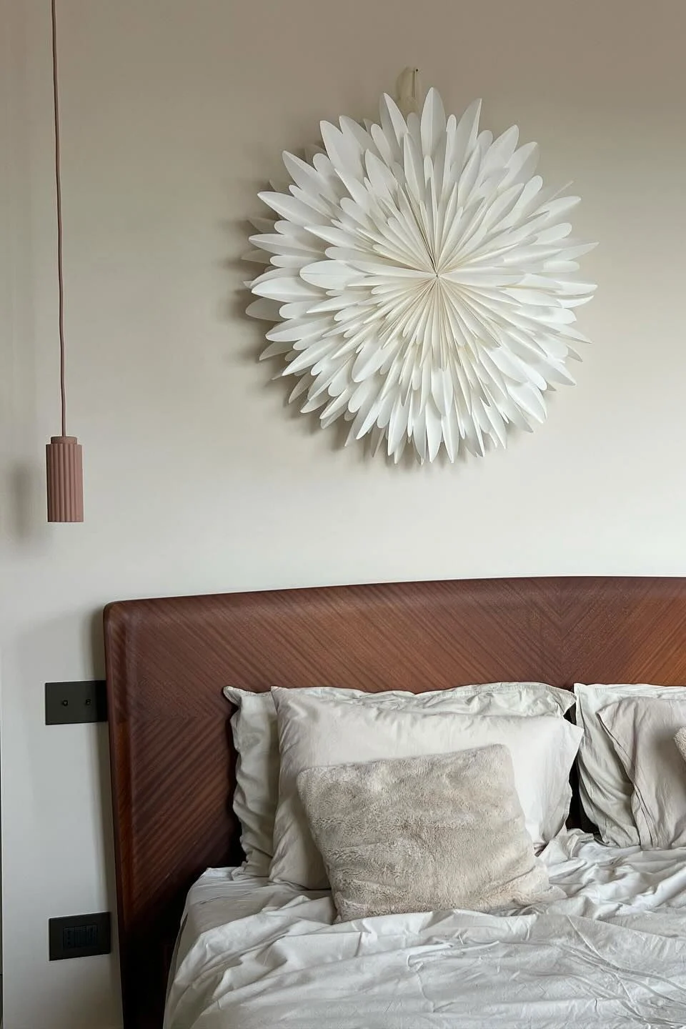 Dormitorio con cama, cabecero de madera, ropa de cama blanca, almohadas mullidas, dos lámparas colgantes y una decoración de pared de estrella de papel blanca.