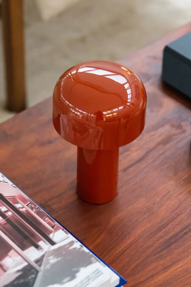 Lámpara de seta naranja brillante sobre una mesa de madera, con una revista en primer plano.