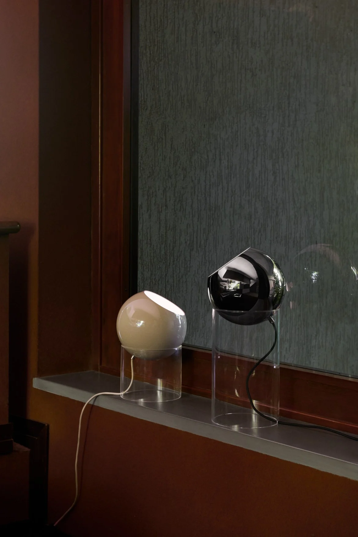 En un alféizar, se encuentran dos lámparas de mesa Topan de &Tradition en diferentes tamaños, una en beige y otra en negro.