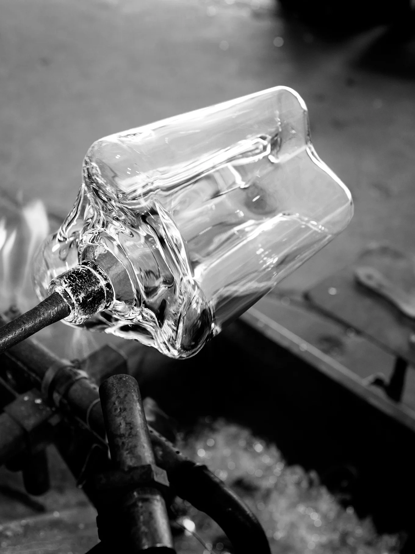 Vaso de cristal transparente moldeándose en varilla de metal con calor, blanco y negro.