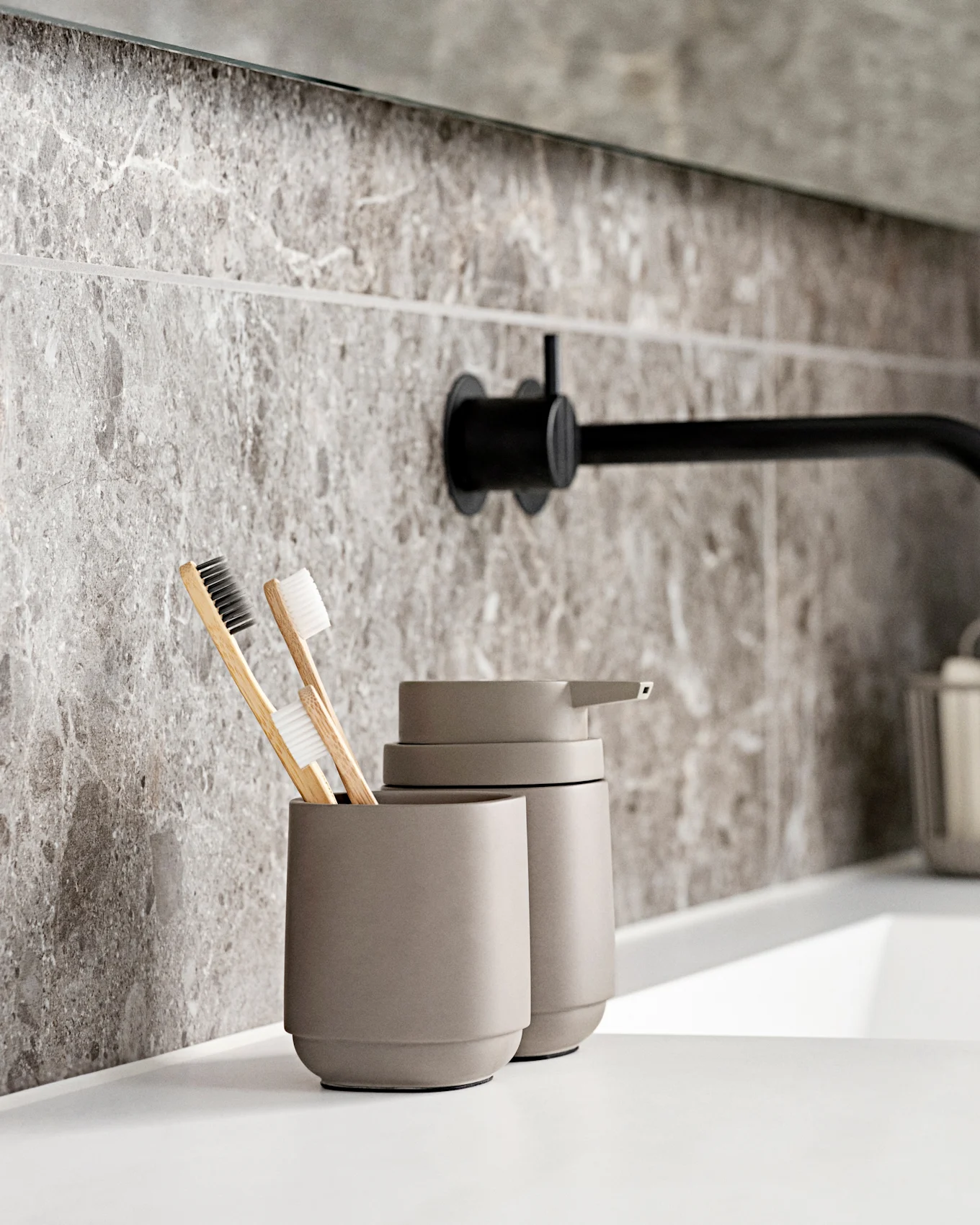 Baño moderno con lavabo blanco, grifo de pared negro, azulejos de mármol gris y cepillos de dientes ecológicos.