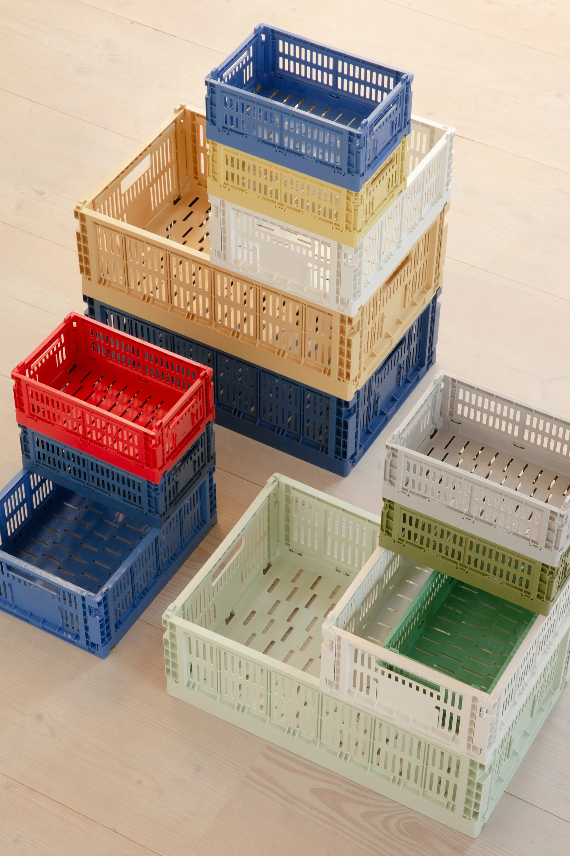 Pilas de cajas plegables de plástico perforado y colorido sobre un suelo de madera clara.