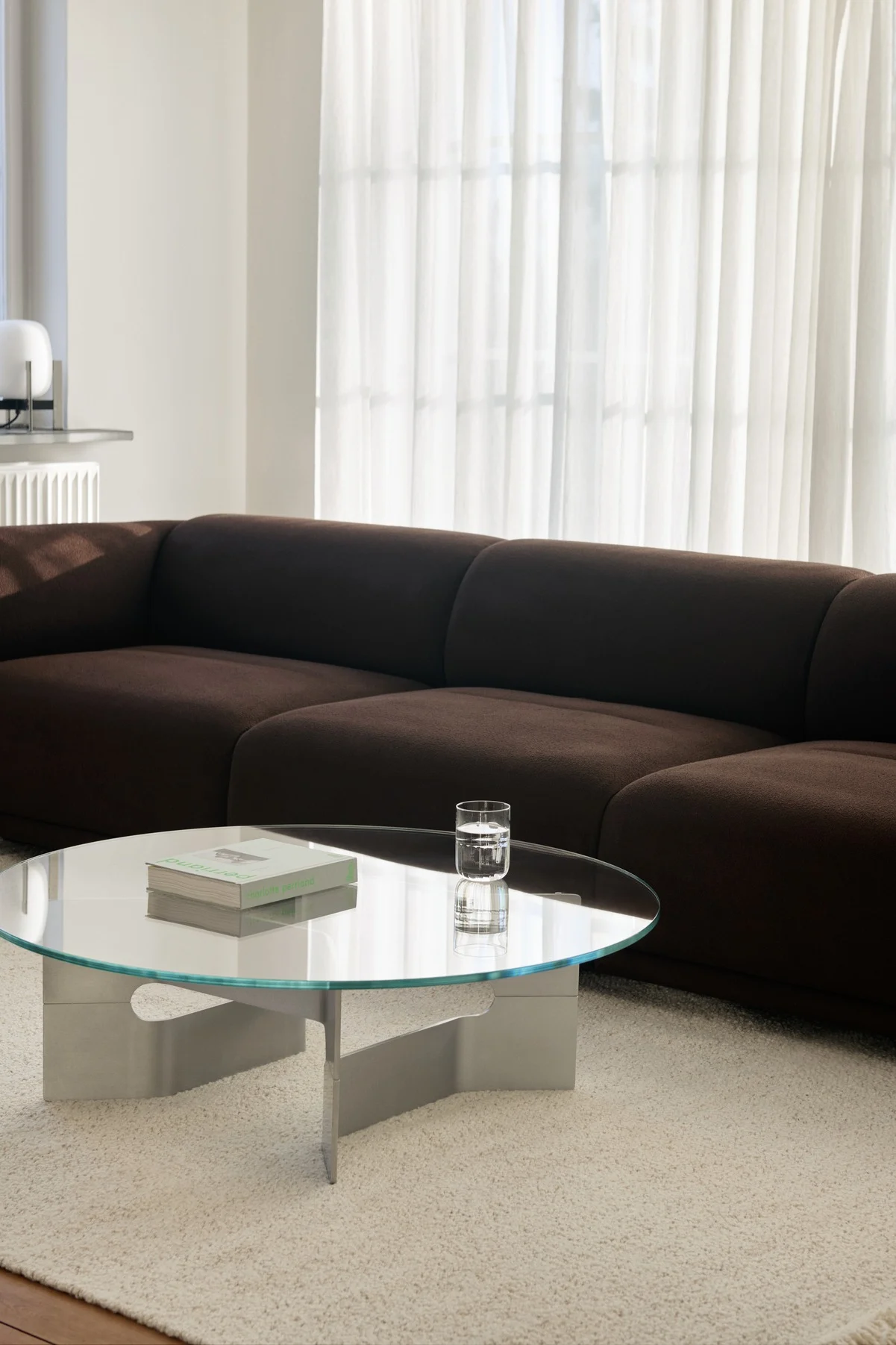 Sala de estar moderna con sofá modular marrón oscuro, mesa de centro de cristal y alfombra clara.