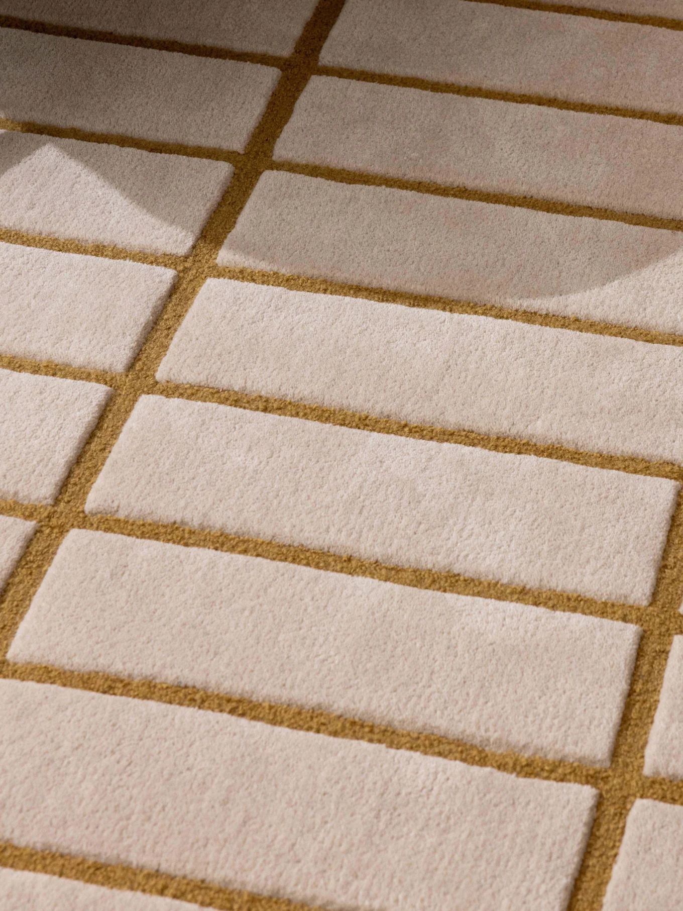 Alfombra con patrón beige y marrón dorado, pata de sillón verde y bandeja con tetera y taza blancas.