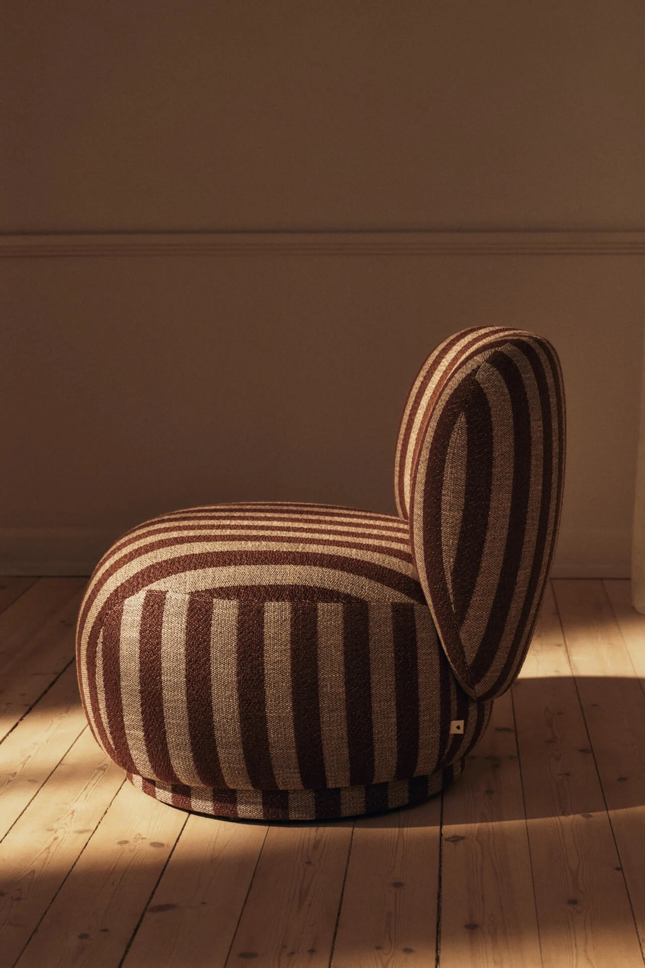Sillón redondeado con rayas marrones y beige sobre un suelo de madera.