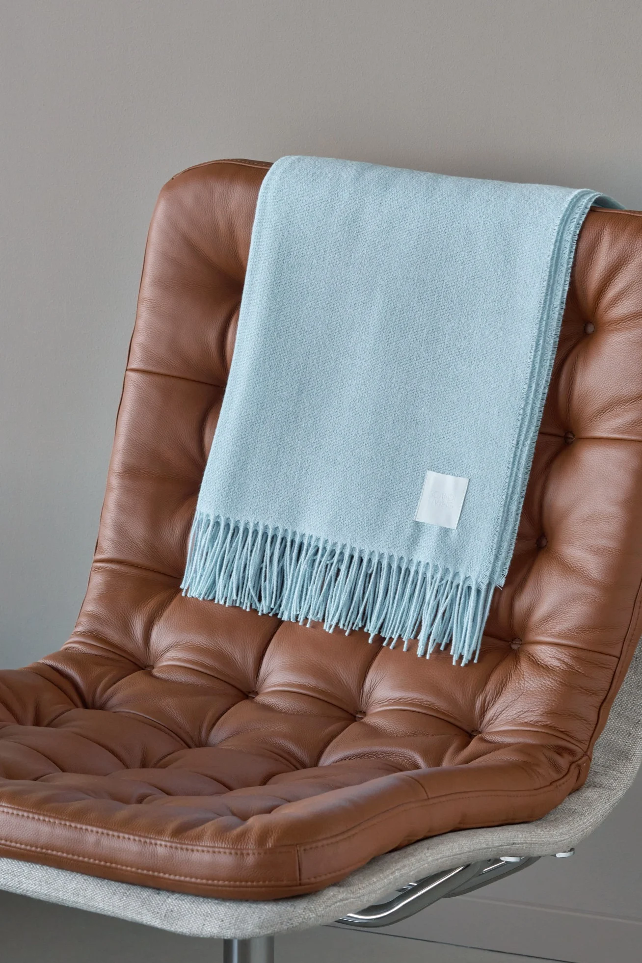Una manta azul claro con flecos sobre un sillón de cuero marrón.