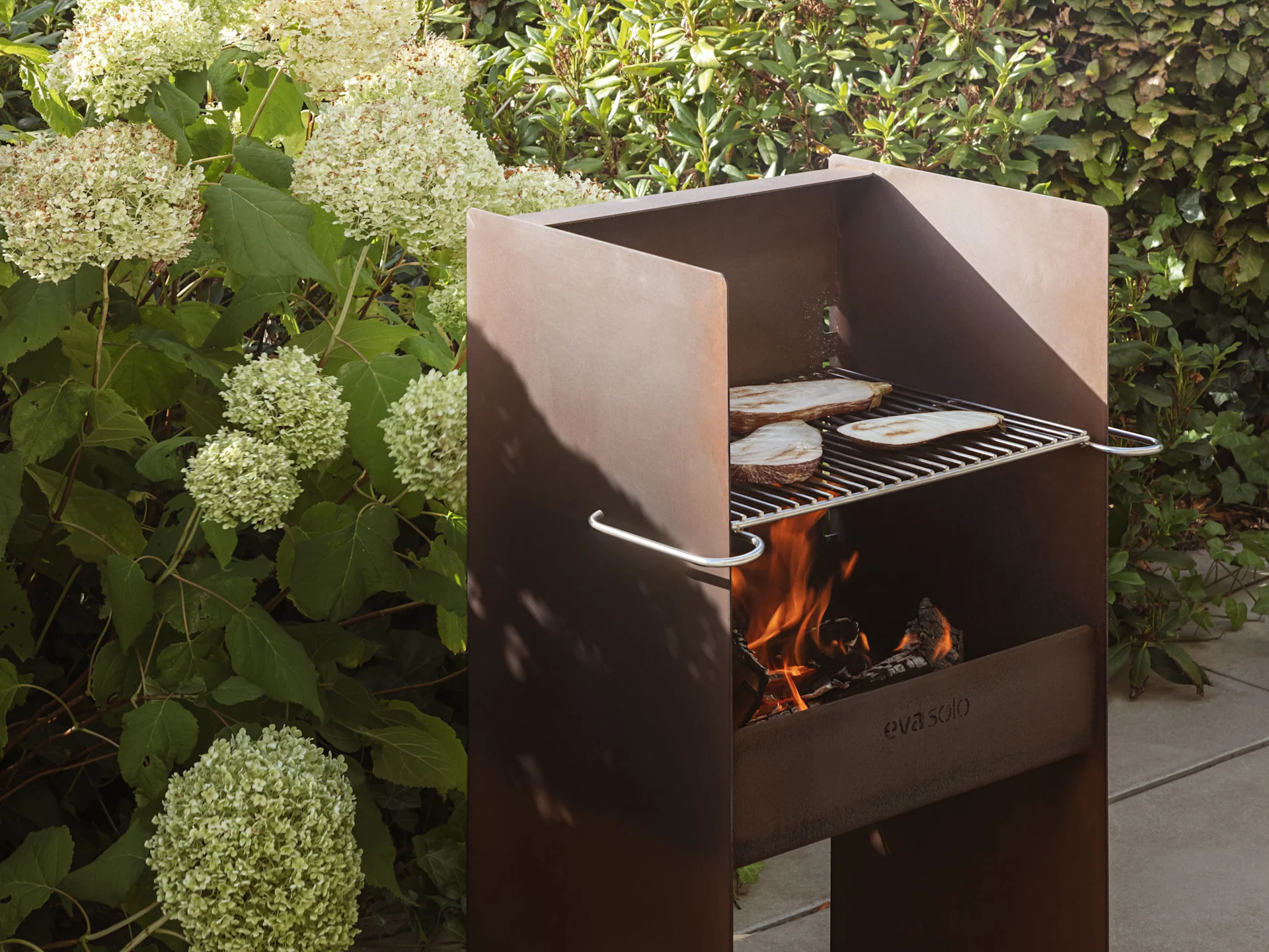 Una parrilla rústica de metal al aire libre con llamas y rodajas de berenjena cocinándose en la rejilla.