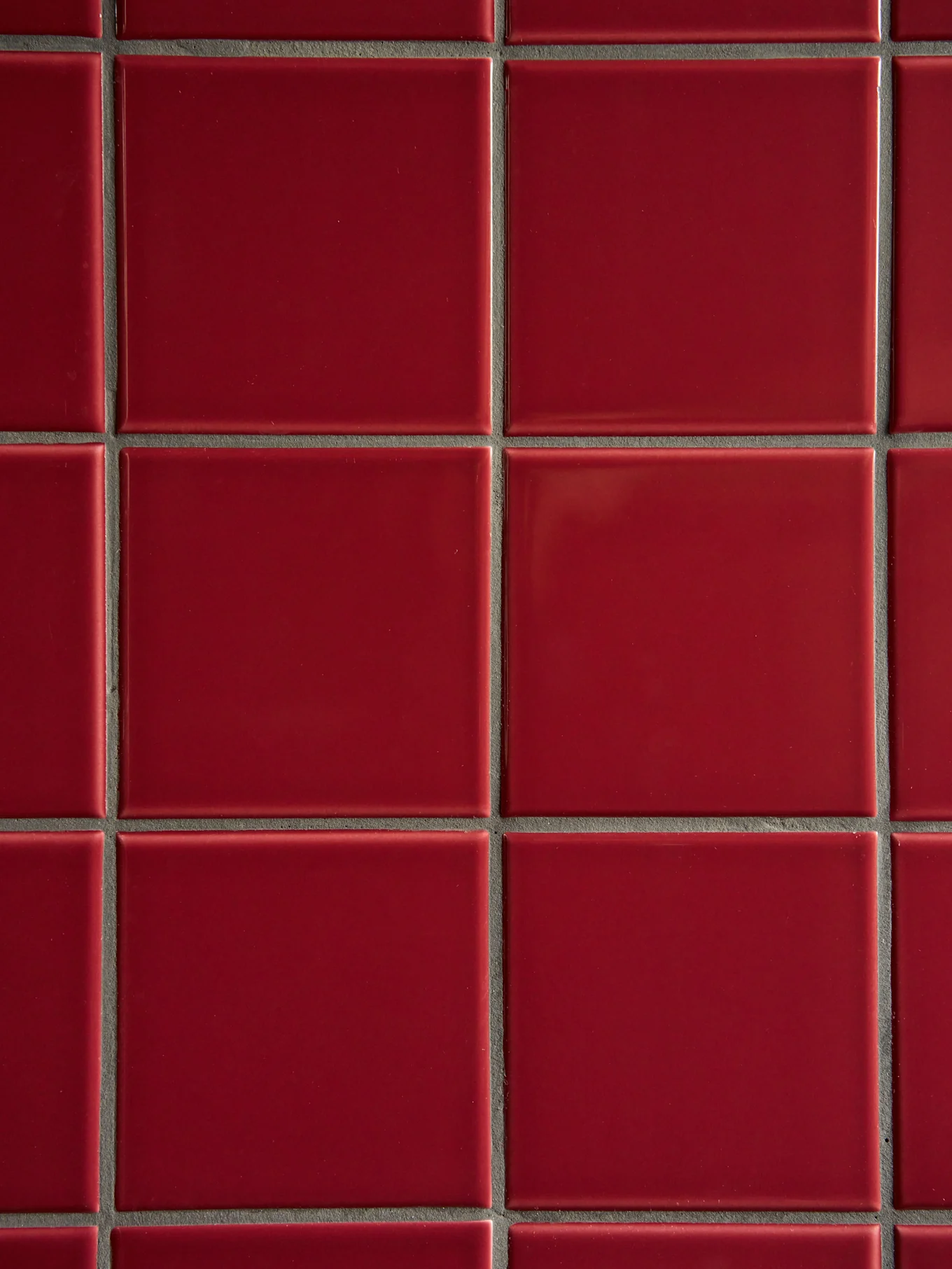 Una cuadrícula de azulejos rojos cuadrados y brillantes con lechada gris oscuro.
