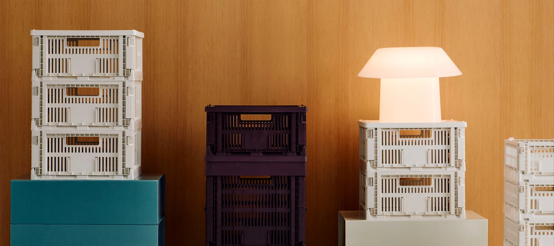 Pilas de cajas plegables blancas y morado oscuro con una lámpara moderna blanca brillante sobre un fondo de madera.
