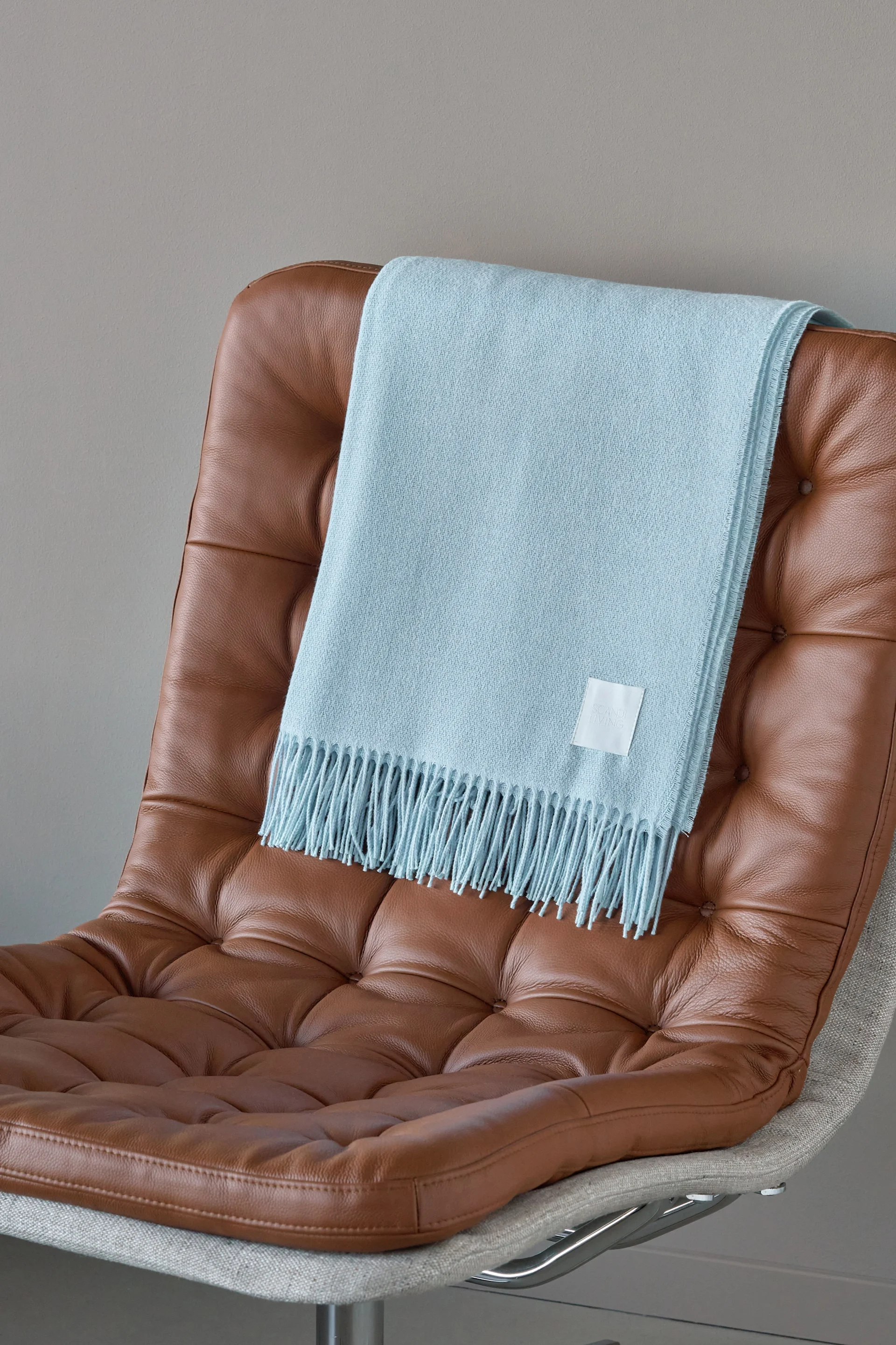 Manta azul claro con flecos sobre un sillón de cuero marrón con botones.