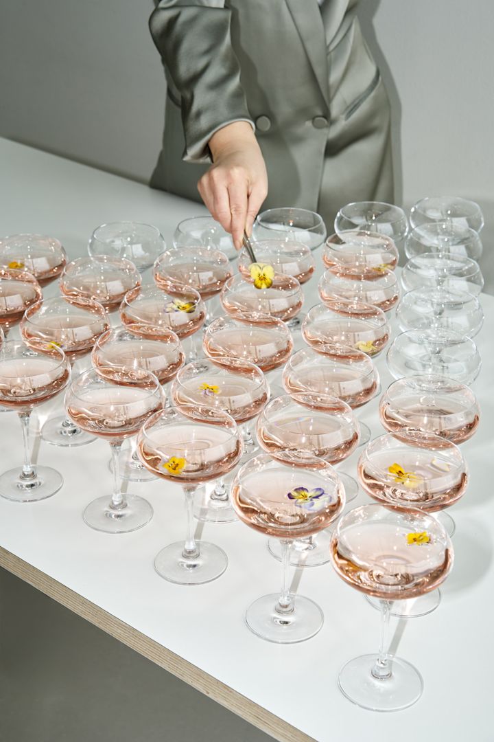 Descubre cómo organizar una fiesta memorable que todos recordarán. En esta imagen, se muestra una mesa llena de bebidas de bienvenida servidas en las elegantes copas More de Orrefors, ideales para darle un toque de distinción a tu evento.