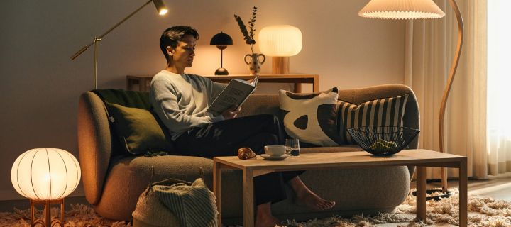Elegir la bombilla adecuada es importante para la sensación que se tiene en casa: un hombre sentado en un sofá rodeado de distintas fuentes de luz, leyendo un libro. 