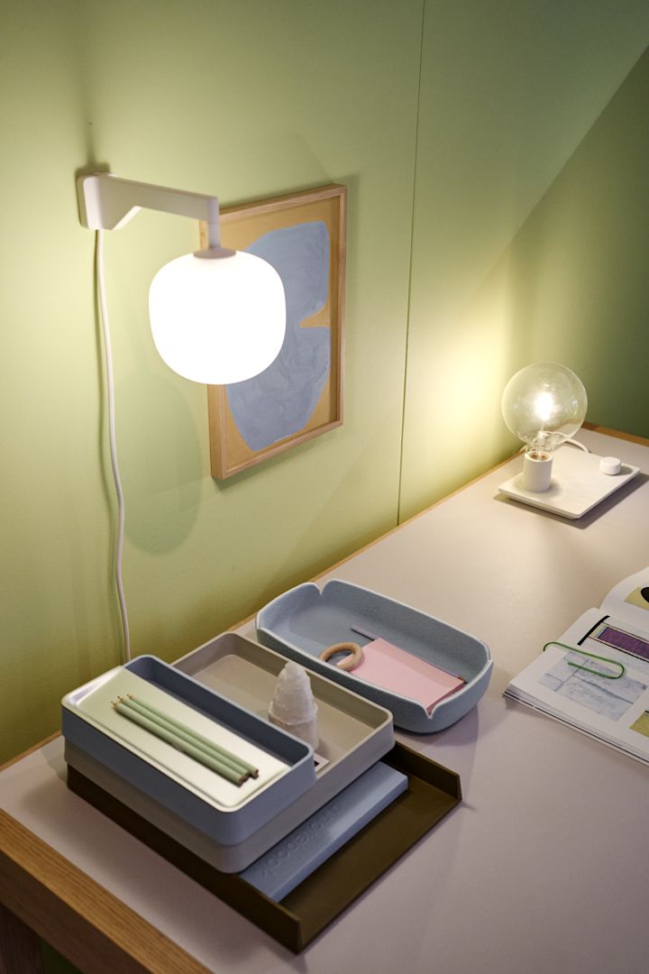 Un escritorio ordenado frente a una pared verde con el aplique Rime de color beige de Muuto.