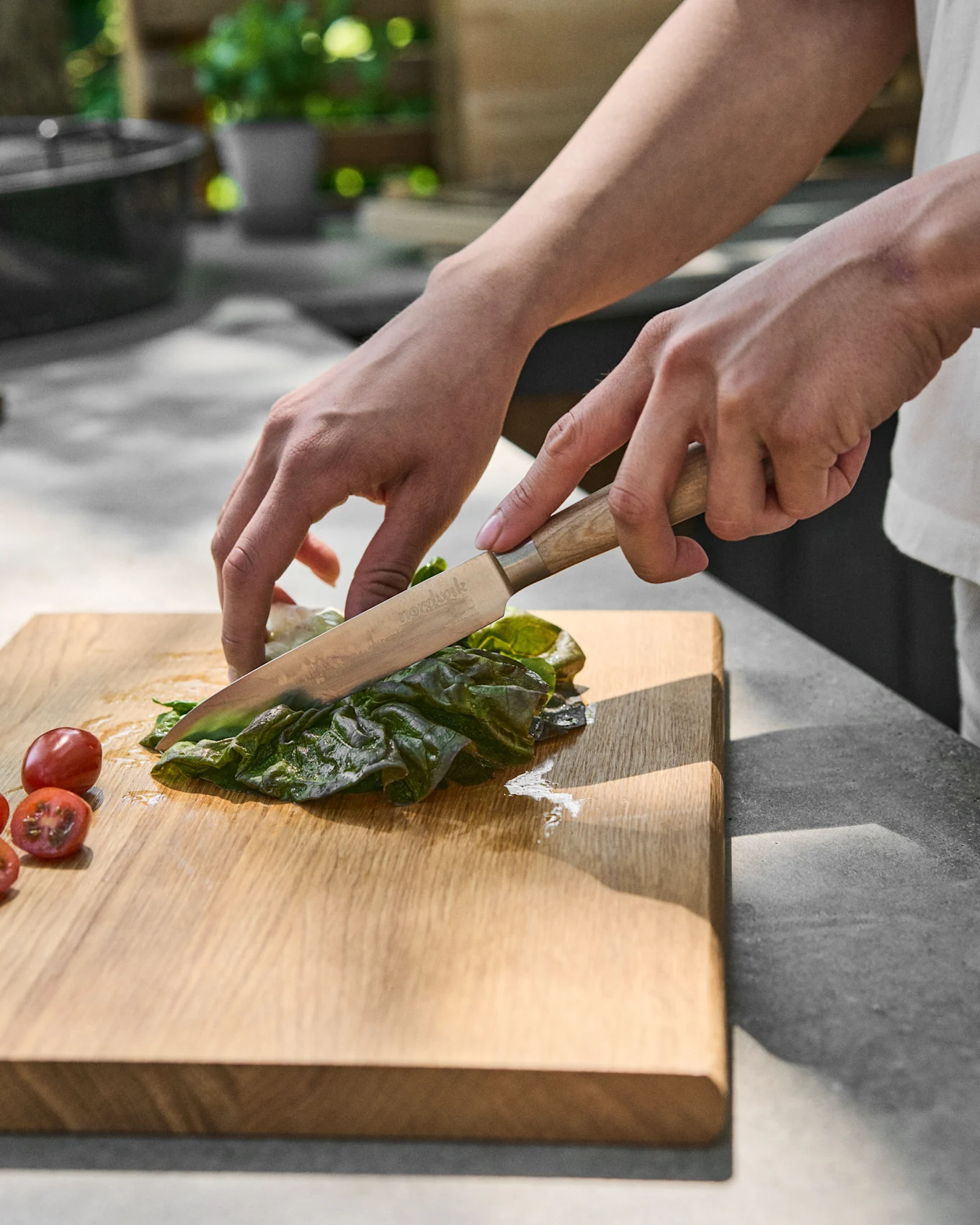 Manos cortando lechuga verde en una tabla de cortar de madera junto a tomates cherry.