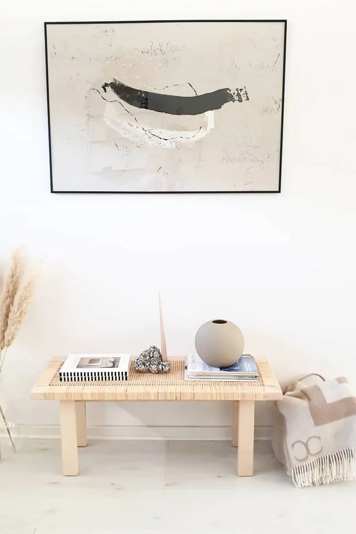 Japandi: Aquí puedes ver un banco decorado con el jarrón Ball de Cooee Design, al lado hay una manta de Classic Collection y un cuadro encima de él.