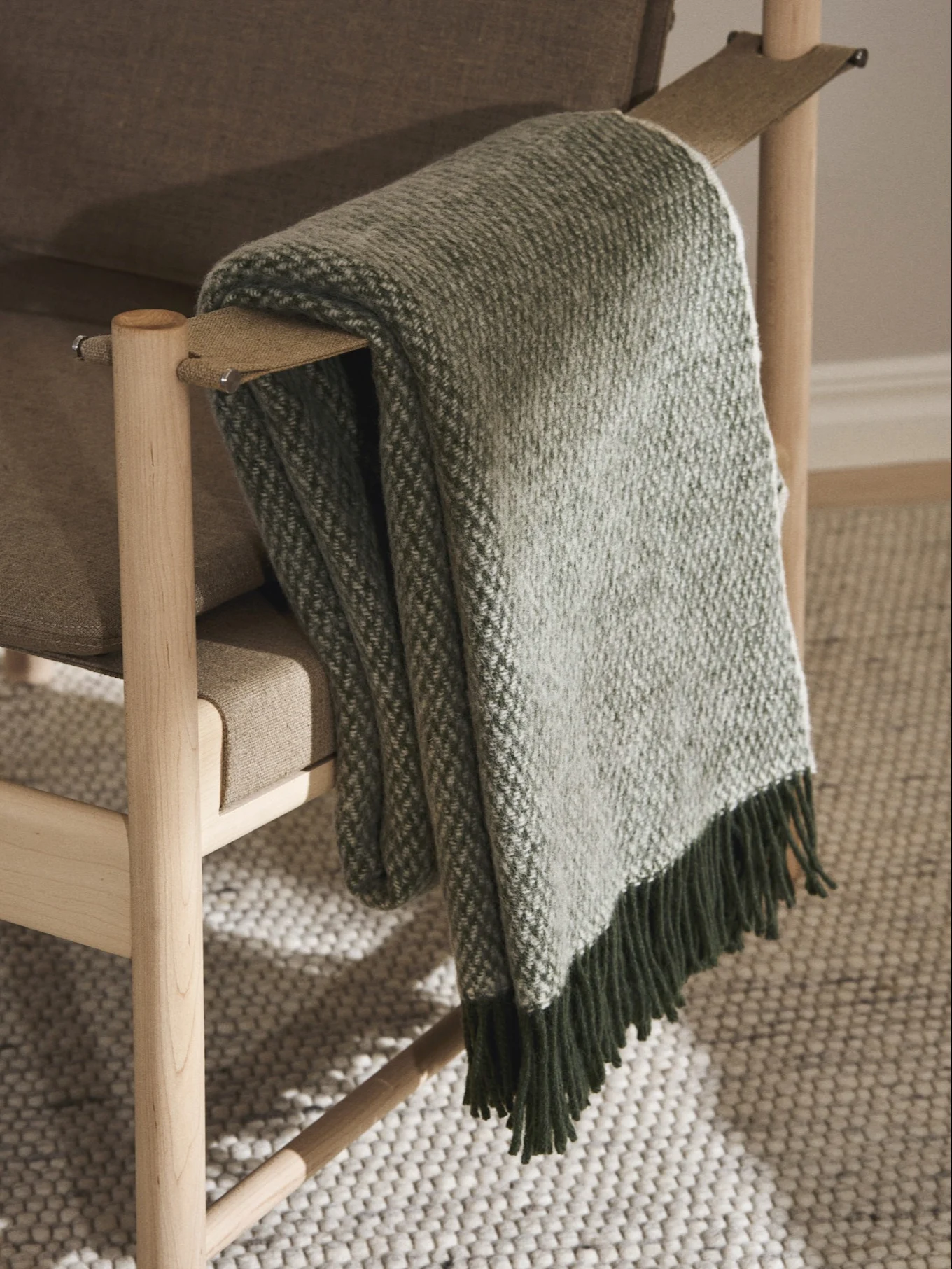 Un sillón de madera marrón claro con una manta de cuadros verdes y blancos sobre el reposabrazos, con flecos verde oscuro.