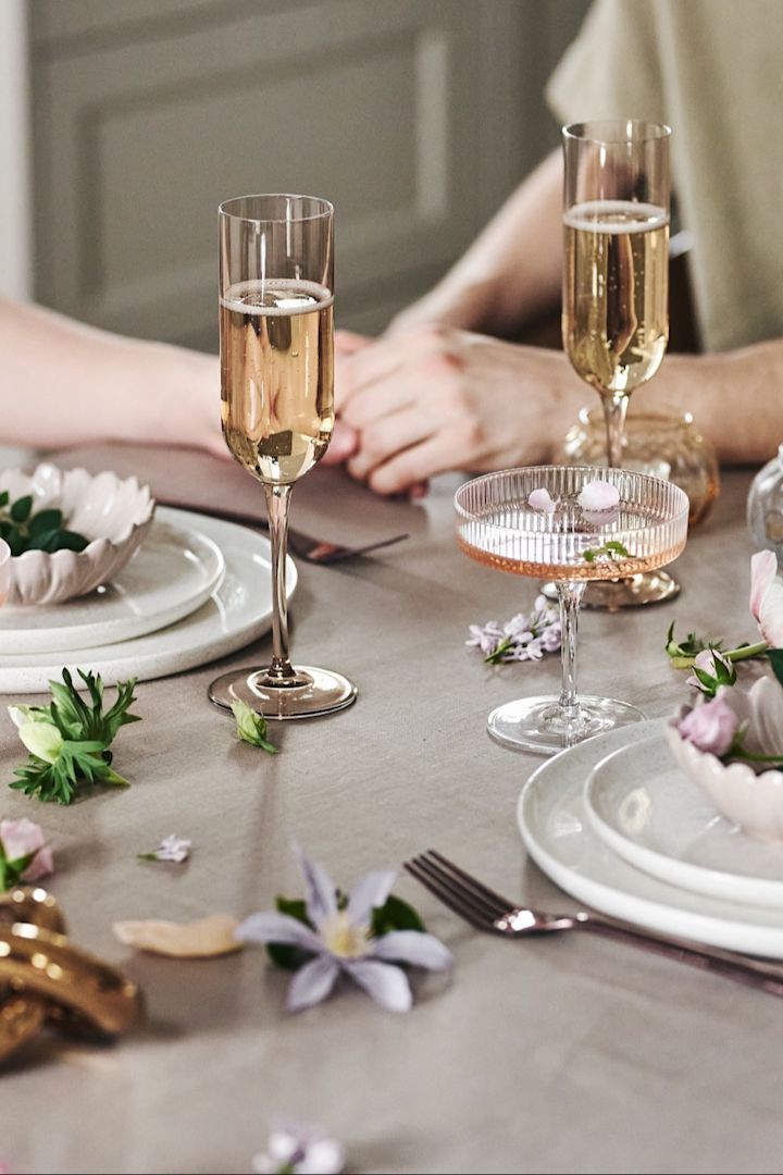 También puedes decorar la mesa de forma divertida para tu comida romántica en casa. Aquí puedes ver vajilla blanca, vasos sencillos y flores sobre un mantel de color beige.