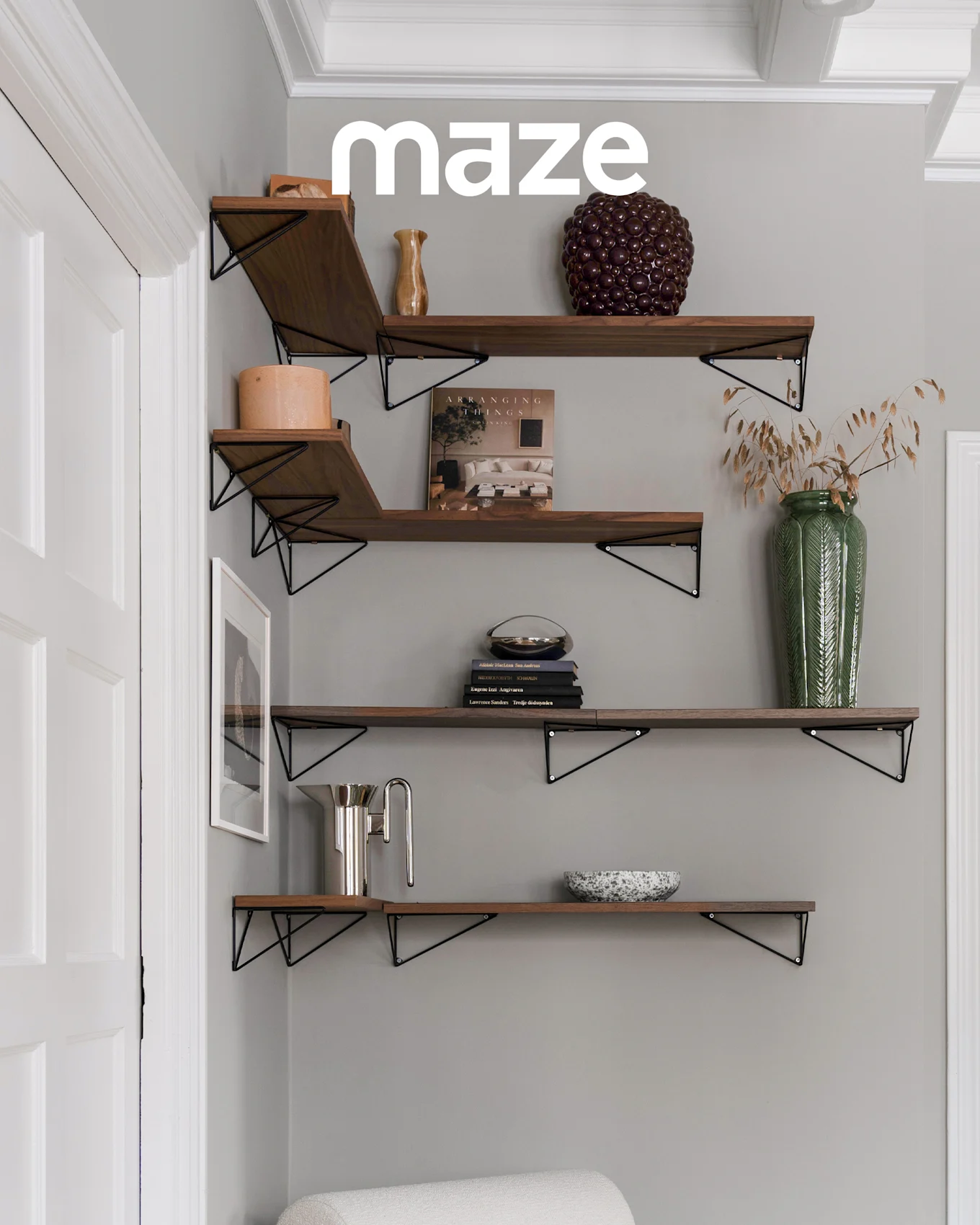Perchero blanco en forma de árbol con pomos de madera en la habitación de un niño con cuna y juguetes. La marca 'maze' es visible.