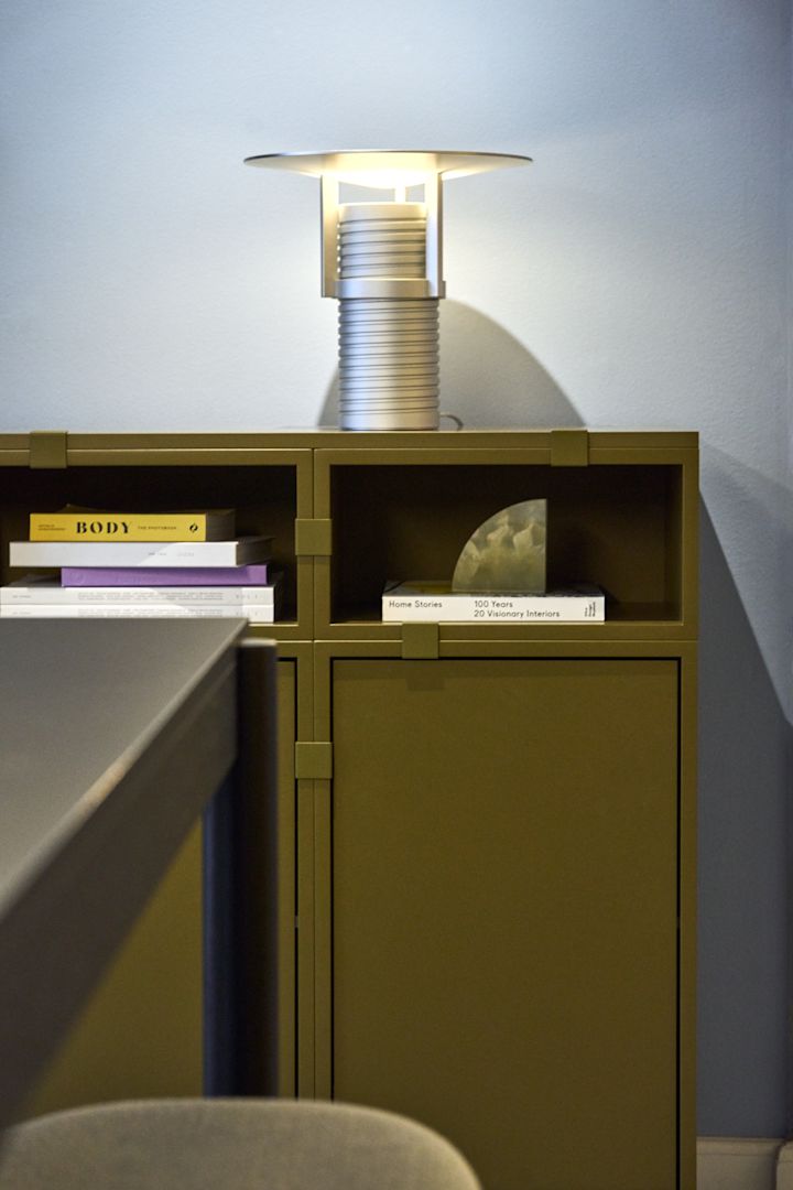 Una estantería verde, de la colección Stacked, con la lámpara de mesa Set plateada encima, todo de Muuto.