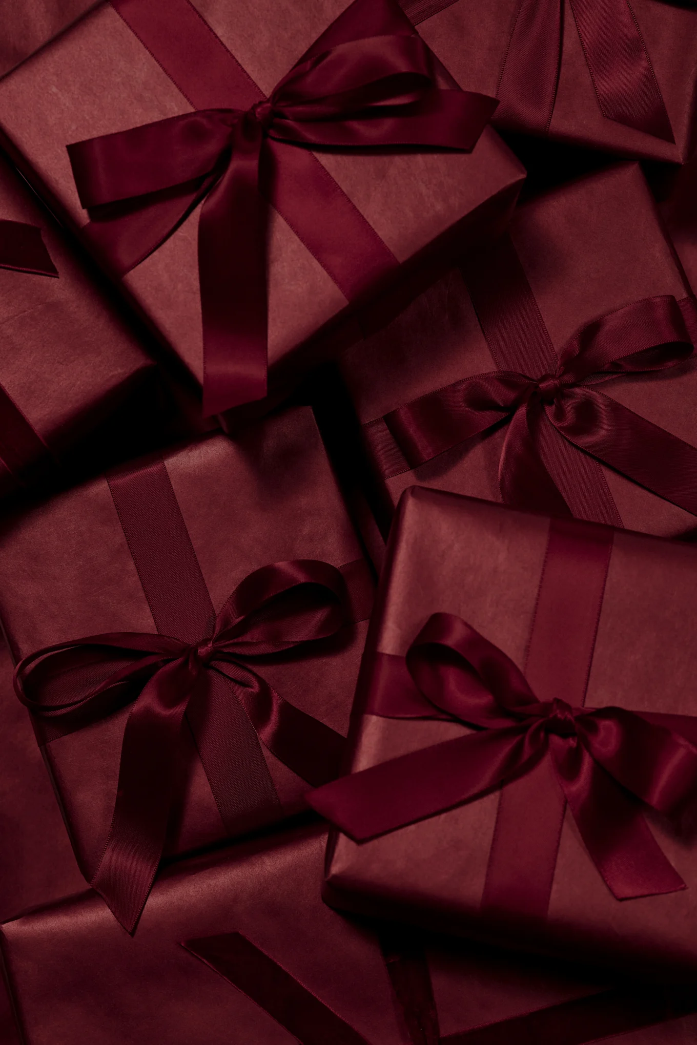 Múltiples cajas de regalo de color rojo oscuro envueltas con cintas y lazos de satén a juego.