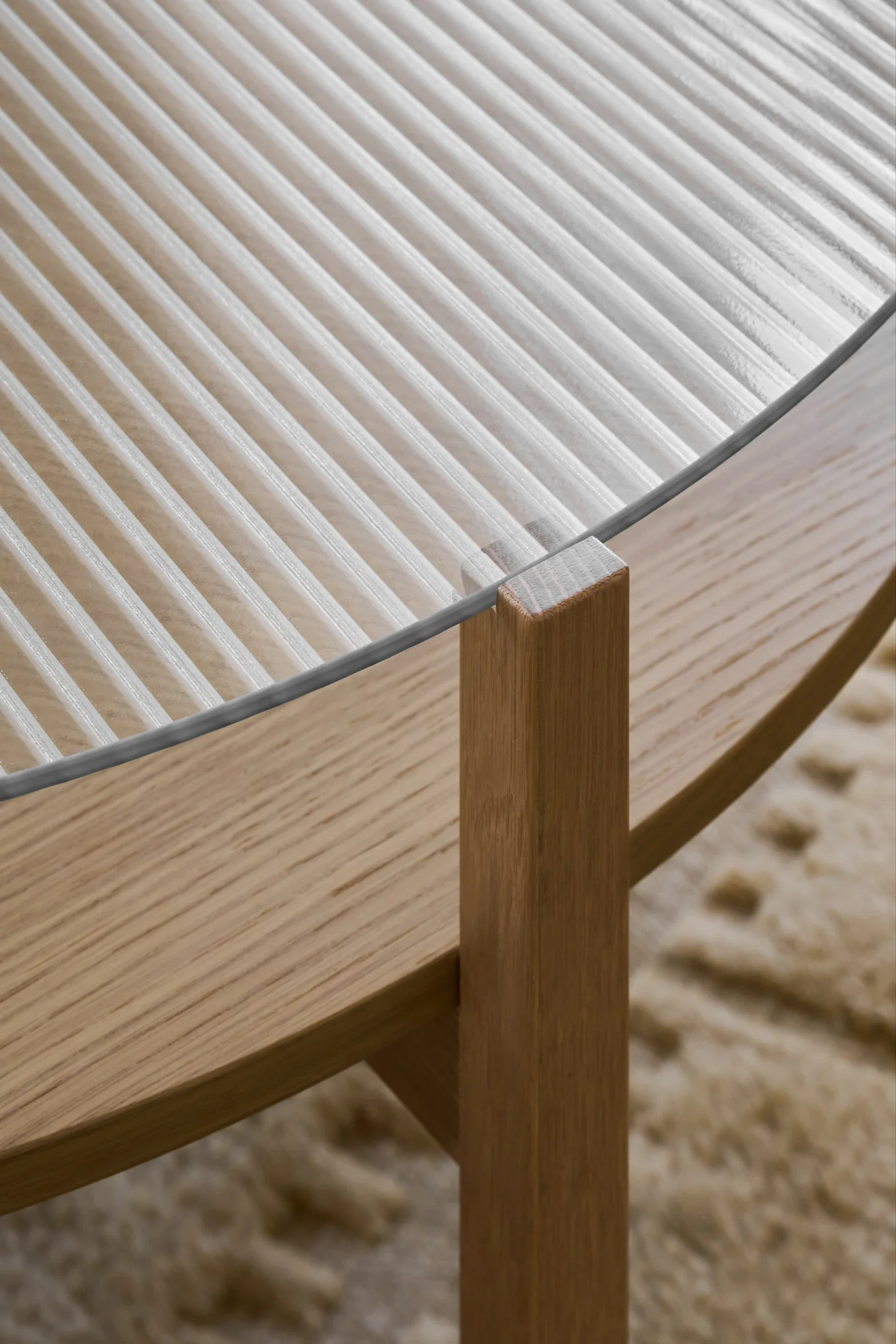 Primer plano de una mesa de centro con tapa de cristal estriado y base de madera clara.