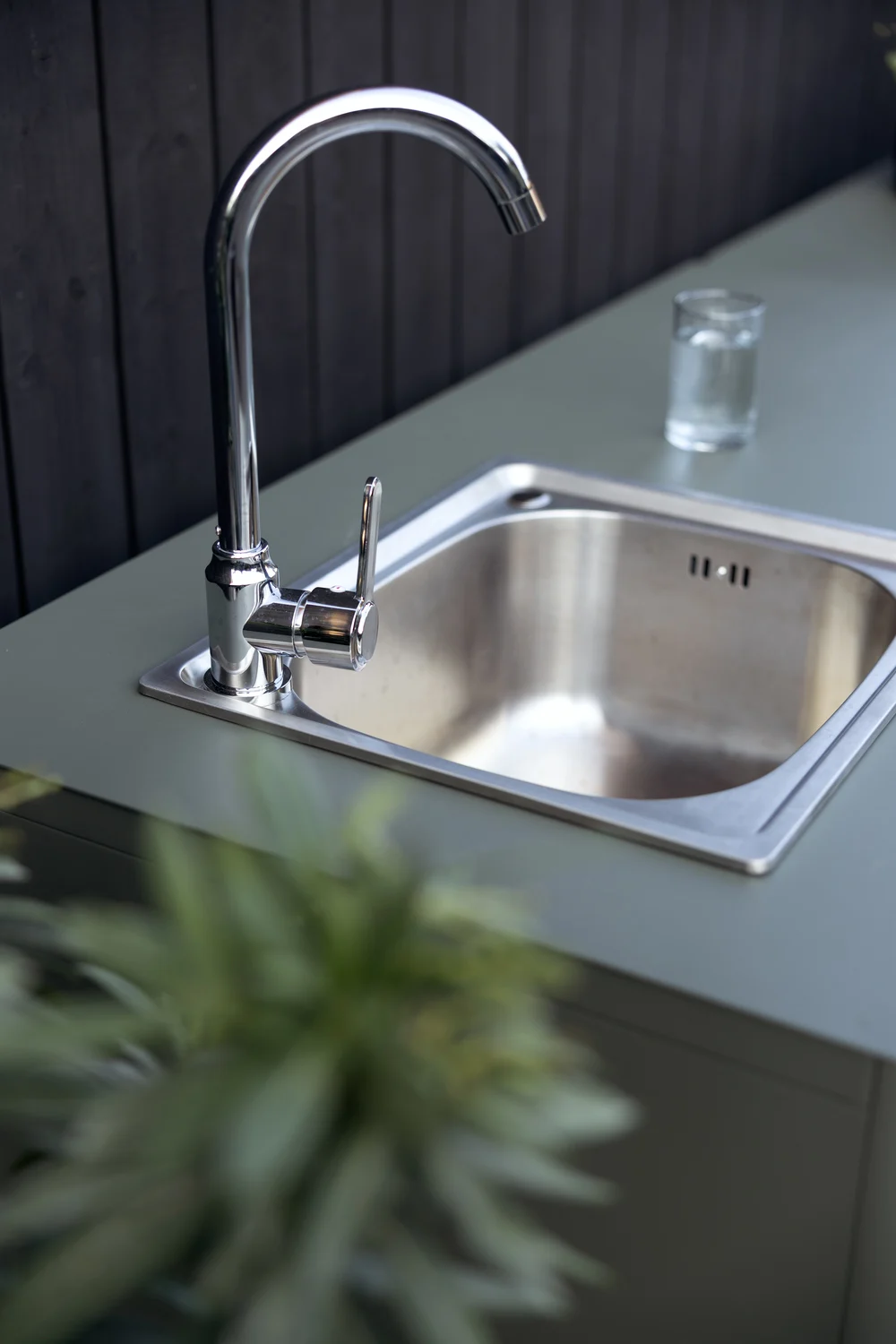 Fregadero de cocina exterior con grifo cromado y un vaso de agua en una encimera verde.
