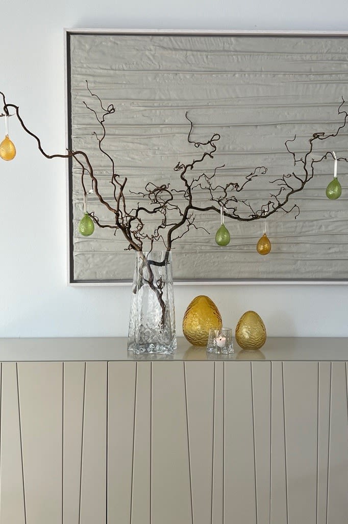 Un ramo de Pascua sobre una cómoda en el jarrón Gry, decorado con colgantes de Pascua Gry, junto a huevos de cristal Gry, todo de Cooee Design.