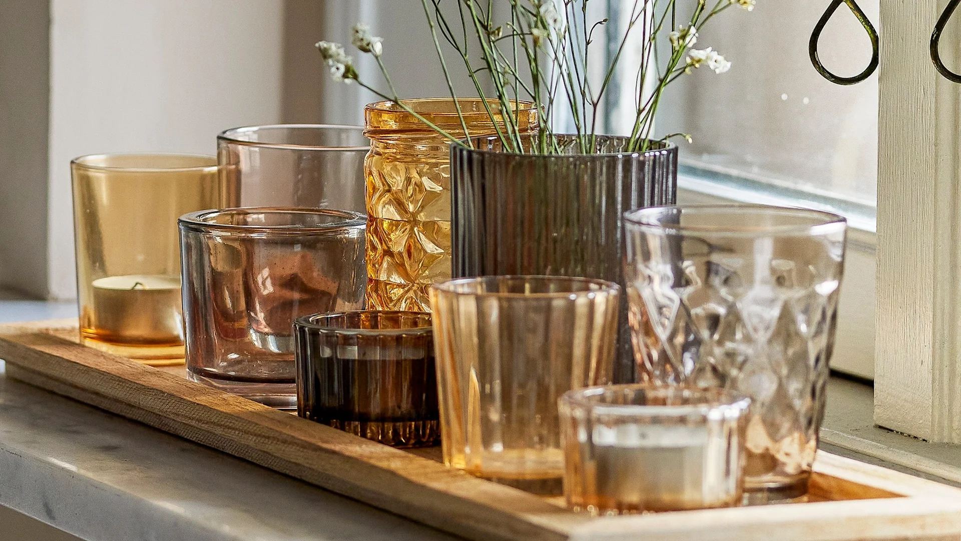 La decoración boho perfecta: la bandeja Sanga con portavelas en varios tonos de amarillo y marrón de Bloomingville sobre el alféizar de una ventana.