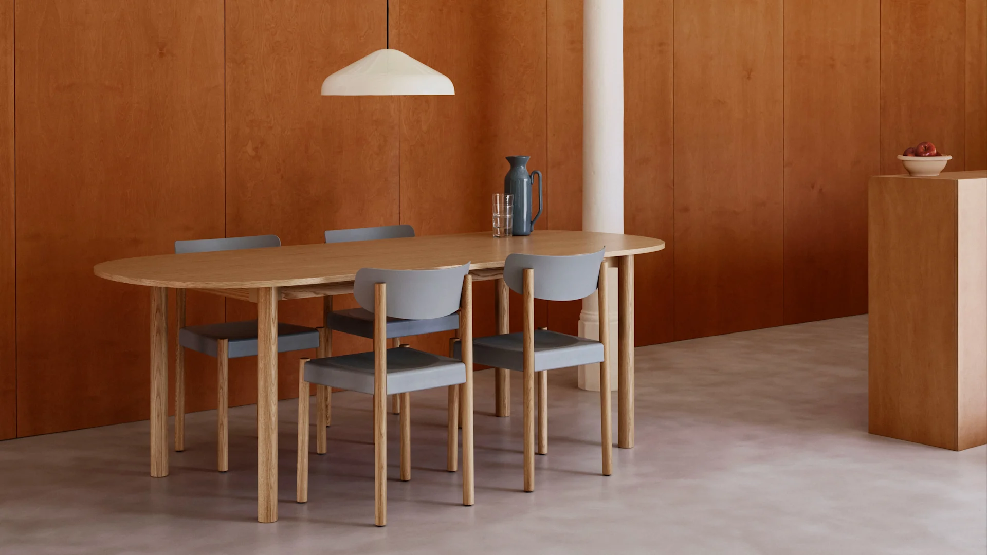 Comedor moderno con mesa de madera ovalada, cuatro sillas grises, paredes de paneles de madera cálida, suelo claro y lámpara colgante blanca.