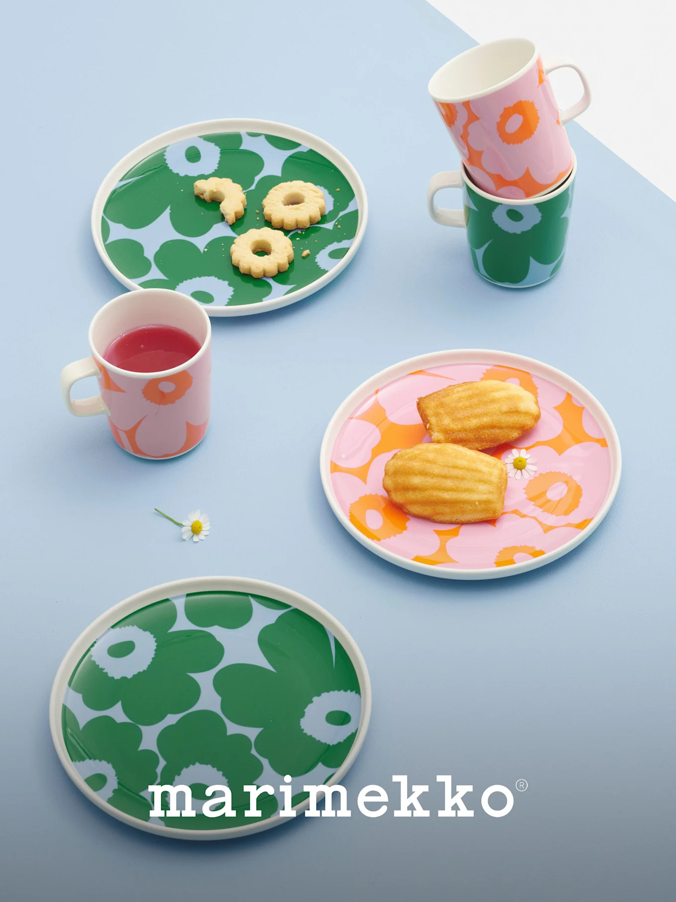 Platos y tazas Marimekko con llamativos diseños florales en verde, rosa y naranja, con galletas, magdalenas y una bebida.