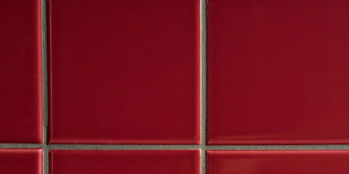 Azulejos cuadrados de color rojo intenso brillante con juntas grises claras en un patrón de cuadrícula.