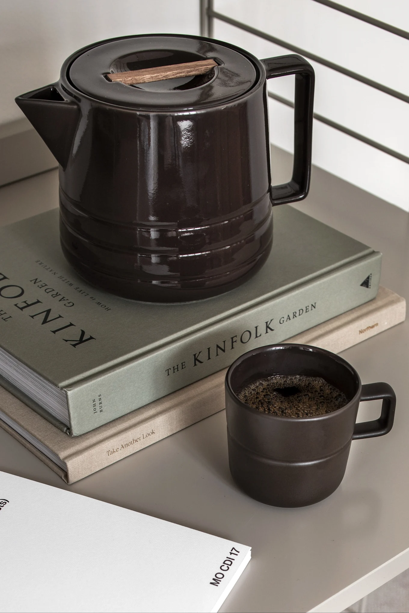Cafetera de cerámica marrón oscuro con detalle de madera, una taza a juego con café y dos libros.