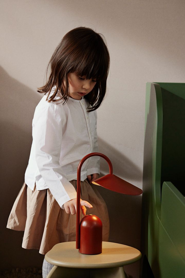 Las lámparas portátiles son una buena idea para decorar las habitaciones infantiles, ya que se pueden mover fácilmente según sea necesario. Aquí la lámpara de mesa portátil Arum en color oxide red de Ferm Living.