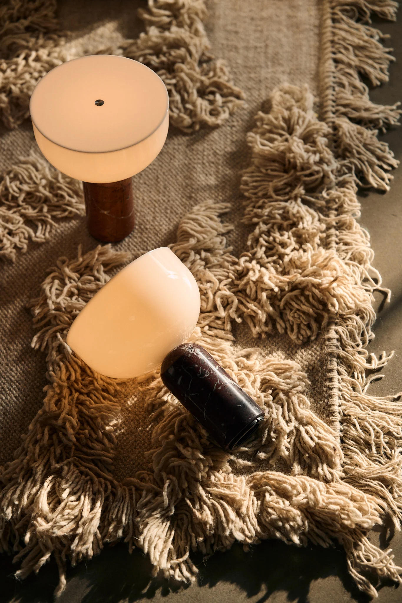 Sobre una alfombra descansan dos lámparas escandinavas: las lámparas de mesa Kizu de New Works.