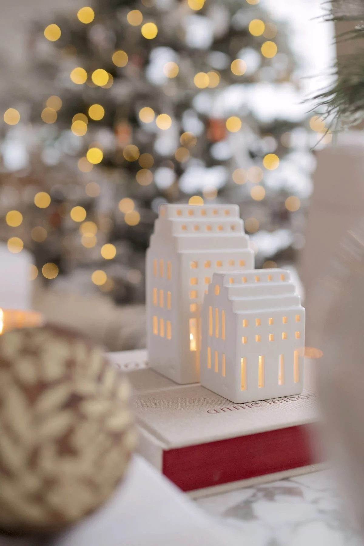 Dos casitas luminosas de la colección Urbania de Kähler están sobre un libro frente a un árbol de Navidad en el hogar de @widveyshome.