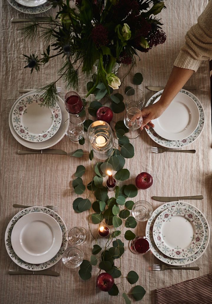 Una idea sencilla y elegante para poner la mesa en Navidad, fotografiada desde arriba con hojas verdes y manzanas rojas como decoración.