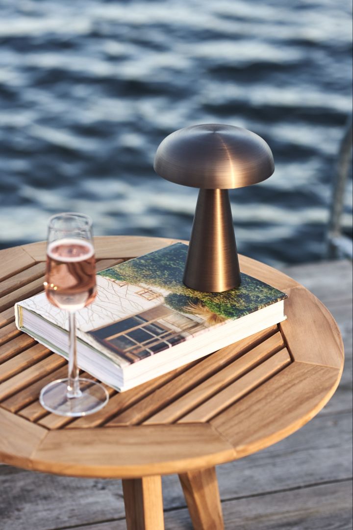 La lámpara de mesa inalámbrica, Como de &Tradition, aquí la vemos sobre una mesa de madera con una copa de vino junto al mar.
