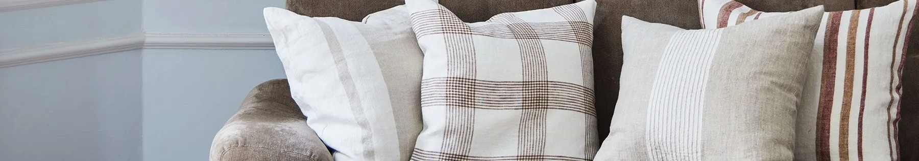 Primer plano de tres cojines en un sofá marrón, con patrones blancos, beige y de cuadros con rayas marrones y rojas.