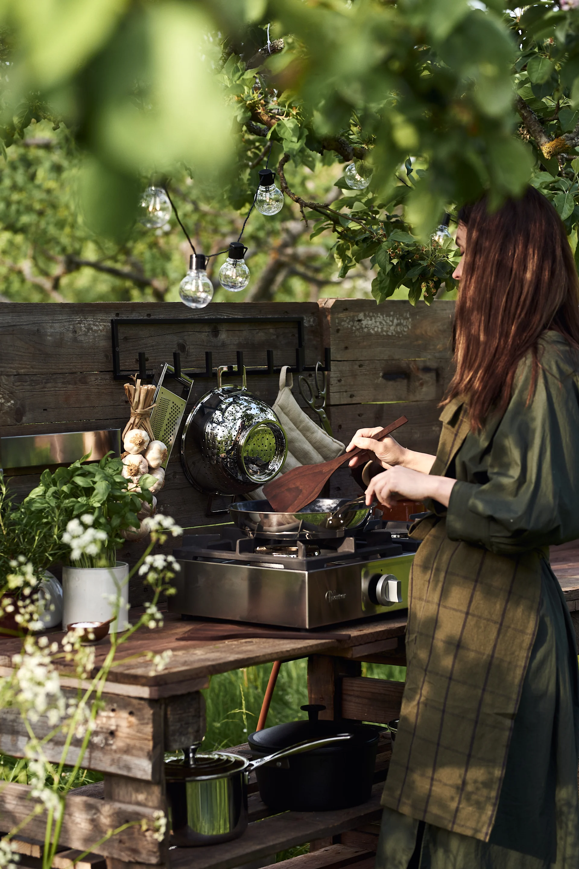 Una mujer cocina en el jardín, en su sencilla cocina exterior de bricolaje hecha con palés.