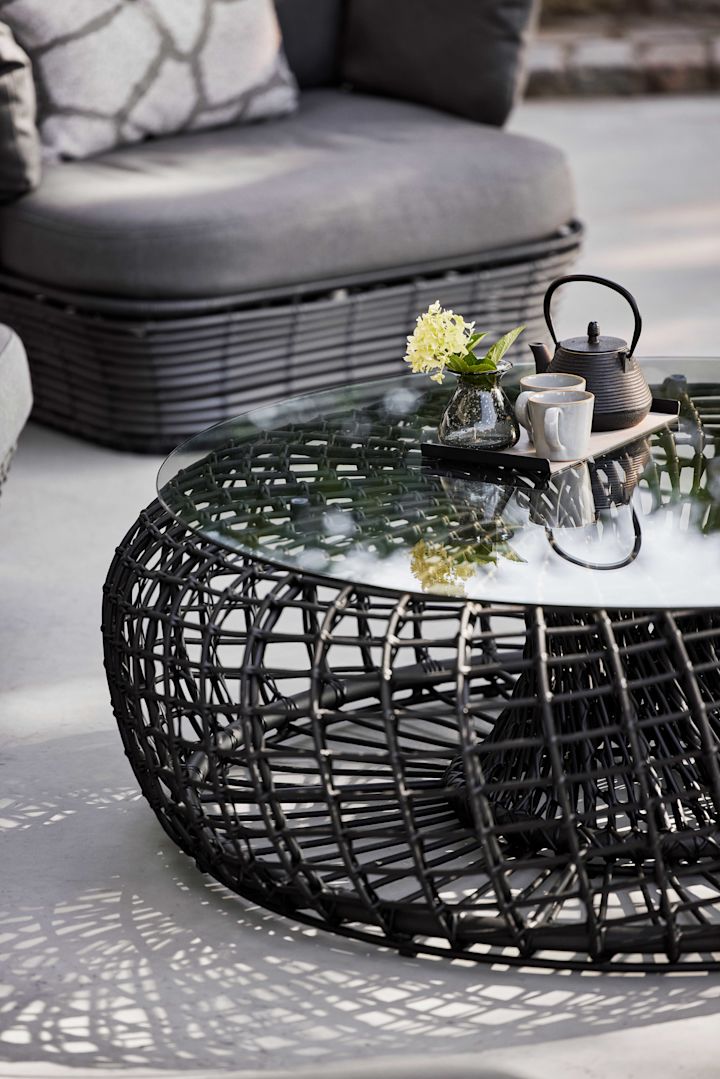 La mesa Nest de Cane-line en negro es de cristal y aluminio e impresiona por su forma redonda, sin duda una tendencia en muebles de jardín para 2025.