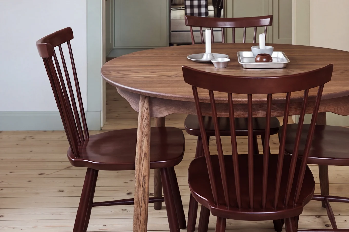 Comedor con mesa redonda de madera, sillas rojas y una lámpara colgante roja, con vista a una cocina con gabinetes verde claro.