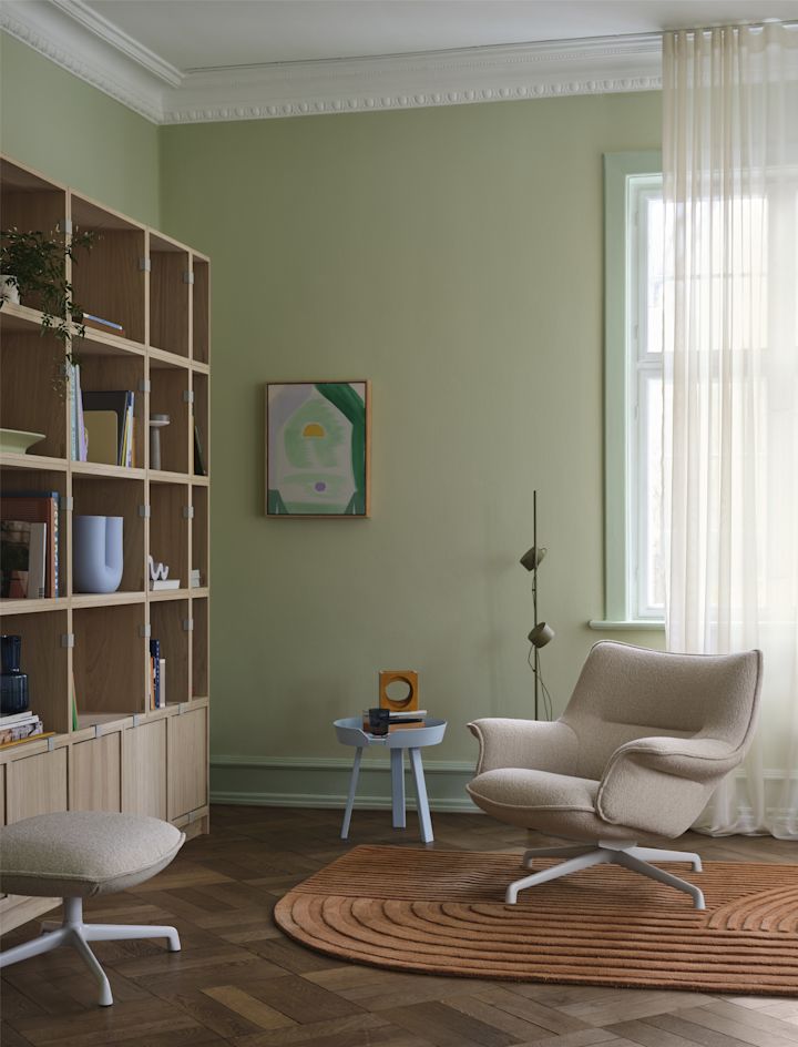 El sillón Doze de Muuto, de color beige, se encuentra frente a una estantería en un salón acogedor.